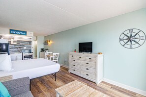 Ein Hotelzimmer mit einem Bett, einem Schminktisch, einem Fernseher, einer Dartscheibe und einer Küchenzeile mit einem Schild, auf dem 'Happy Place' steht.