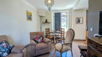 Uma sala de estar com sofá, poltrona e mesa de jantar com cadeiras.