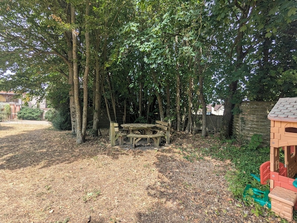 A wooden picnic table surrounded by trees in a backyard.