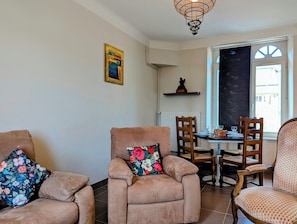A living room with two armchairs, a dining table with chairs, and a window with a view.