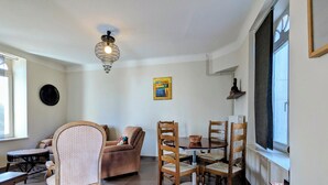 Un soggiorno con divano, tavolo da pranzo con sedie, poltrona decorata, lampadario a soffitto e finestra con tende.