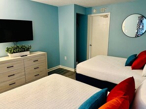 A bedroom with two beds, a dresser, a TV, and a door. - Paradise by the Sea. Oceanfront. (Myrtle Beach)