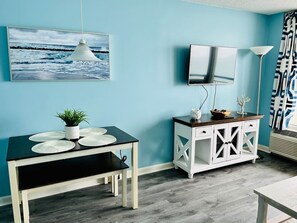 A room with a dining table, a white cabinet, a mounted TV, and a hanging pendant light. - Paradise by the Sea. Oceanfront. (Myrtle Beach)