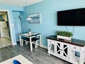 Ein Zimmer mit Esstisch, Stühlen, Fernseher und einem Schrank mit einer Pflanze.