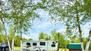 A campsite with a recreational vehicle, a red chair, and a fire pit. - Junction 19 & Co - Upper Site #2 - Full Service RV / Tent Camping Site (Fort Kent)