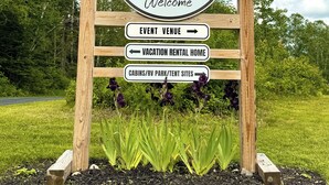 A welcome sign for Junction 19 & company with directional arrows for event venue, vacation rental home, and cabins/RV park/tent sites. - Junction 19 & Co - Upper Site #2 - Full Service RV / Tent Camping Site (Fort Kent)