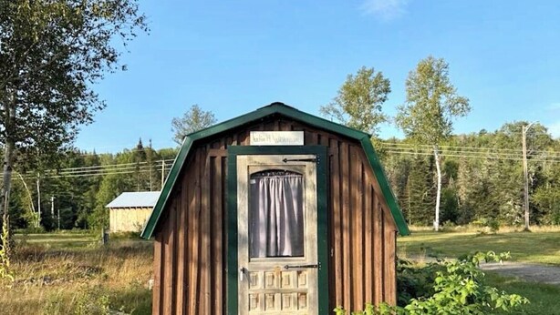 A small wooden structure with a door and a window, surrounded by grass and trees. - Junction 19 & Co - Upper Site #2 - Full Service RV / Tent Camping Site (Fort Kent)