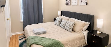 Un dormitorio con cama, mesitas de noche, ventilador de techo, ventana con cortinas y decoración en la pared.