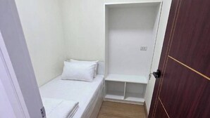 A small, narrow room with a single bed, a built-in shelf, and a wooden door. - Hotel Backpack   BTS Punnawithi PKK2 (Bangkok)