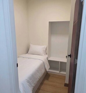Ein kleines Zimmer mit einem Einzelbett, Holzboden, einem weißen Bett und einem weißen Nachttisch.