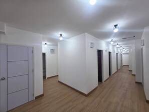 Ein langer, schmaler Gang mit weißen Wänden und Holzboden, der zu mehreren Türen führt.