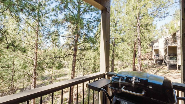 A covered outdoor area with a grill, overlooking a forested landscape and a building with balconies. - 1BR Condo w/Game Room, Pool & Hot Tub (Bend)