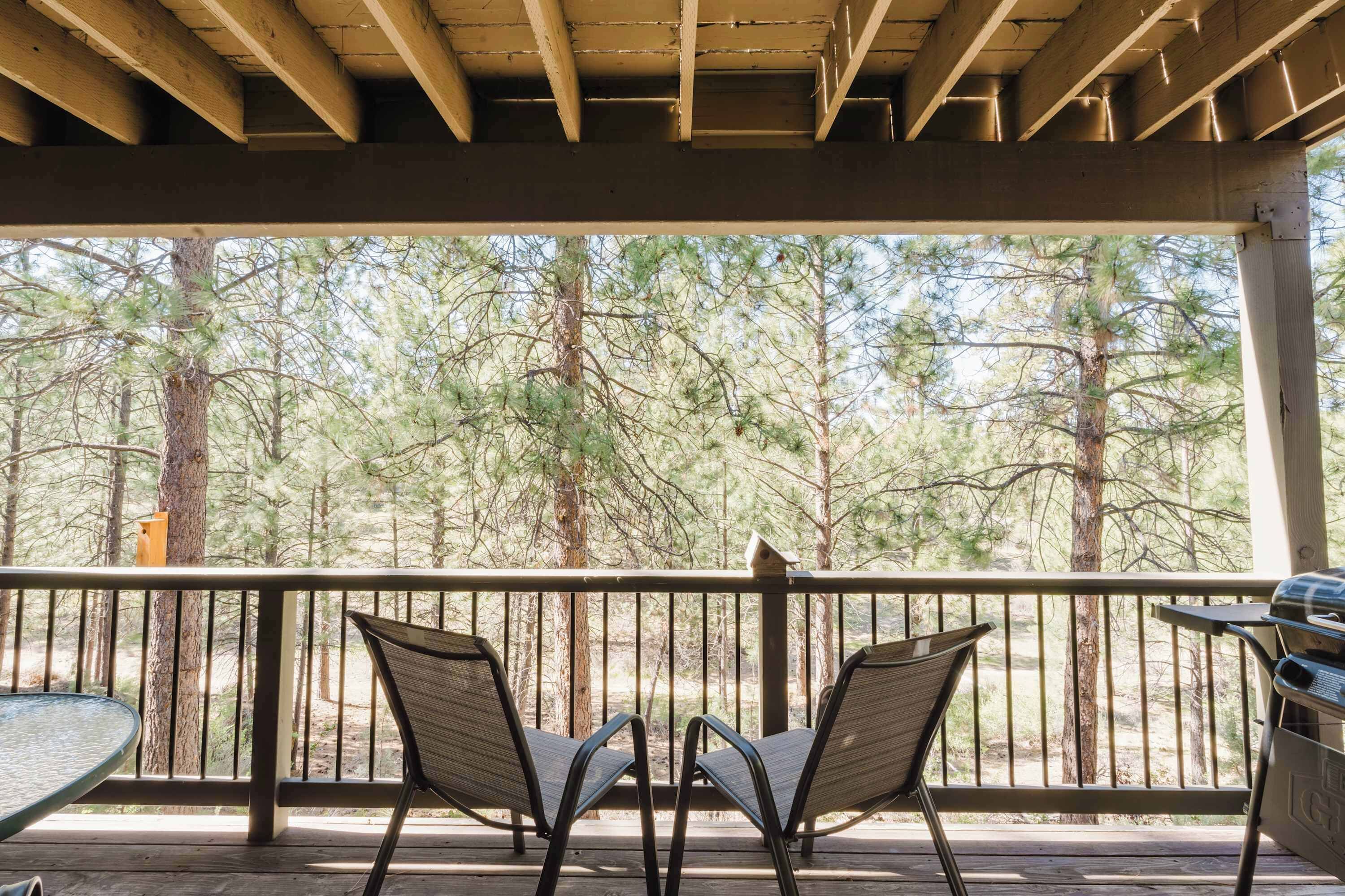 Ein überdachter Außenbereich mit zwei Stühlen, die auf einen Wald Blick werfen, einem Grill und einem Tisch.