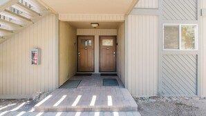 A building entrance with a covered walkway leading to two wooden doors, each marked with a number. - 1BR Condo w/Game Room, Pool & Hot Tub (Bend)