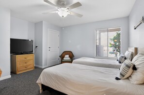 A bedroom with two beds, a ceiling fan, a television on a wooden dresser, and a window with blinds. - Courtside 67 - Your Perfect Hilton Head Island Getaway (Hilton Head Island)