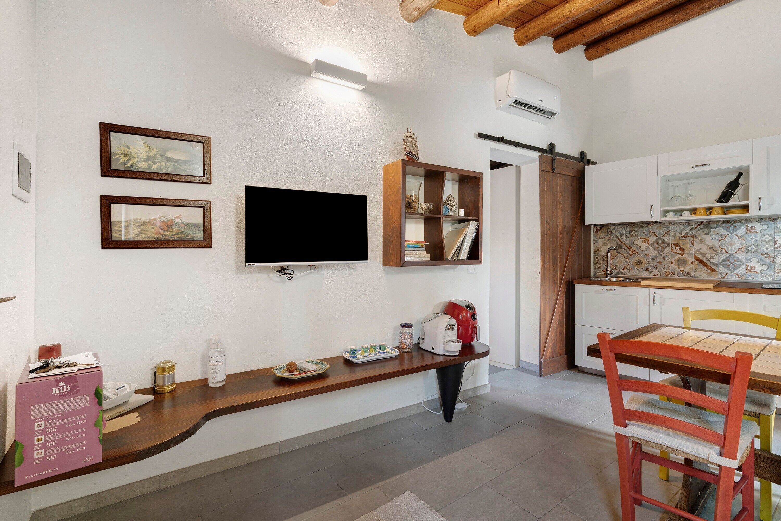 Una cocina compacta con horno integrado, cafetera y comedor con mesa y sillas de madera.