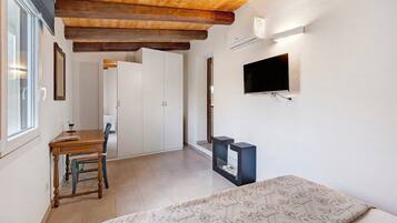 A room with a wooden ceiling, a television mounted on the wall, a bed with a patterned bedspread, and a desk with a chair.