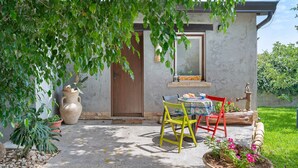 Een terras met een tafel, stoelen, een bloempot en een deur.