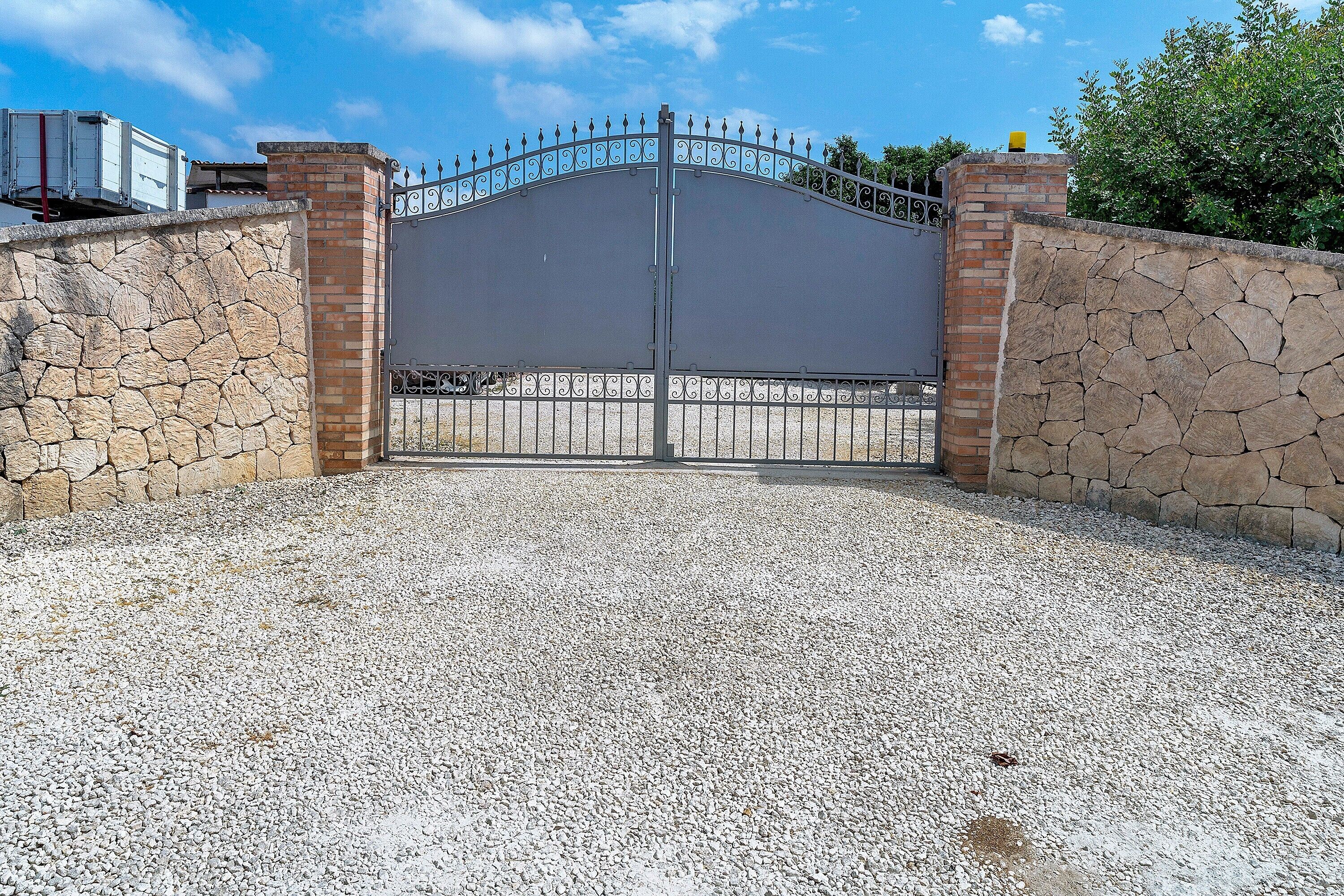 A gated entrance with a metal gate, stone walls, and a gravel driveway.