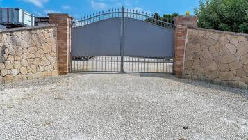 A gated entrance with a metal gate, stone walls, and a gravel driveway.