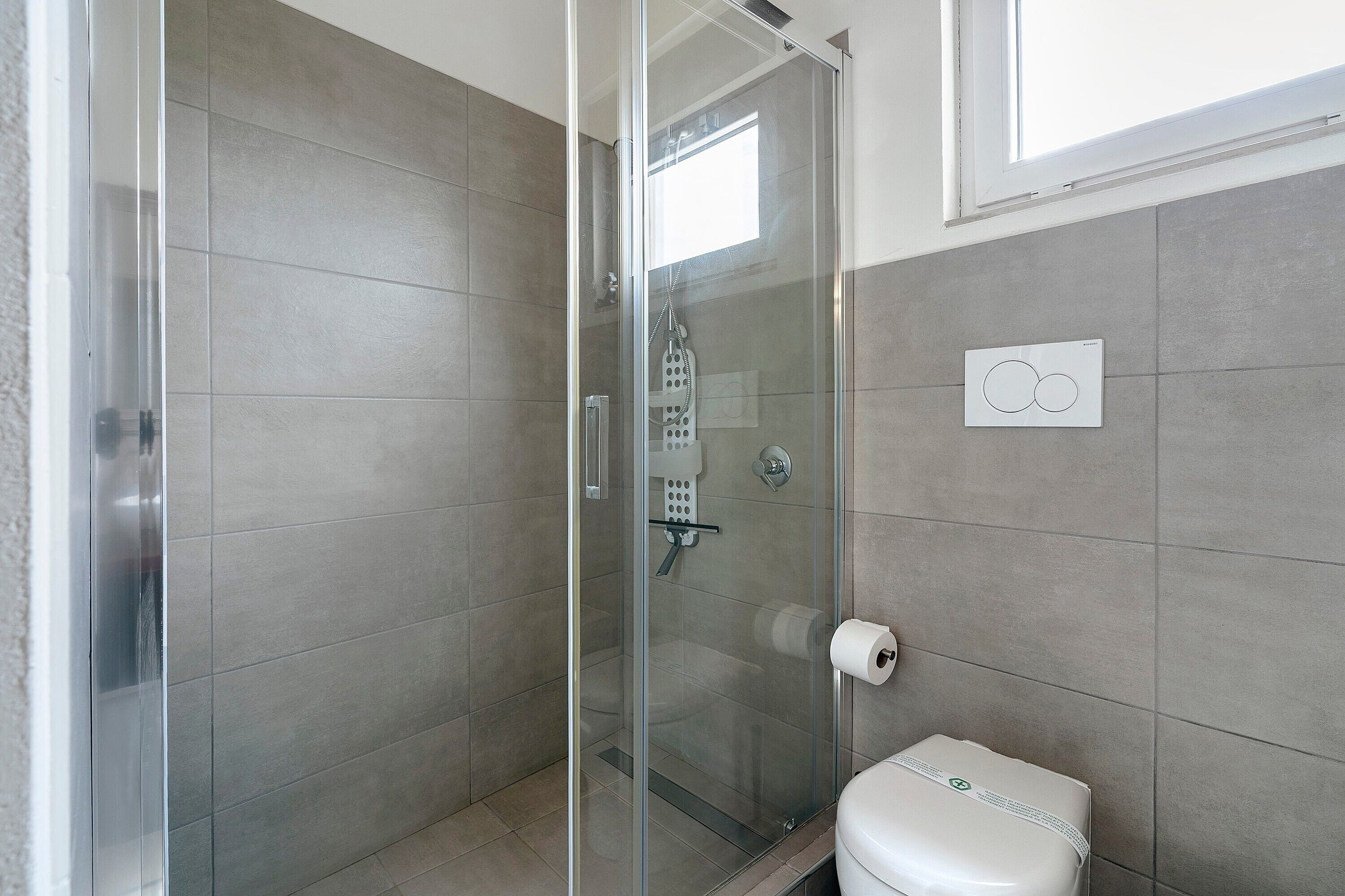 Ein Badezimmer mit Duschkabine aus Glas, Toilette und Bedienfeld an der Wand.