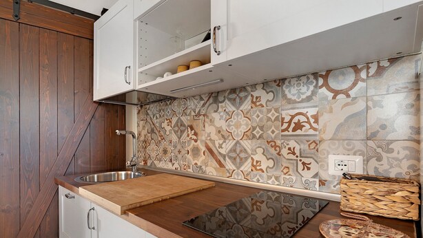 Een keuken met een houten aanrecht, witte kastjes en betegelde spatwand.