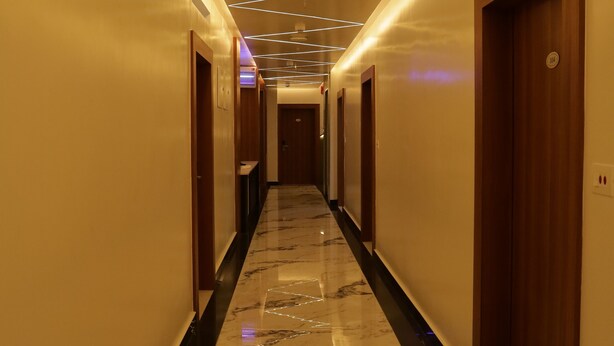 Een hotelgang met een marmeren vloer, houten deuren en moderne verlichtingsarmaturen.