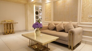 Een moderne woonkamer met een beige bank, een glazen salontafel en een decoratieve vaas met paarse bloemen.