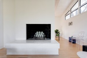 A modern living room with a fireplace, a seating area with clear chairs, and a potted plant. - Aalto Modern - Spacious, 5-bed MCM - A Luxury KY Derby Vacation! (Louisville)