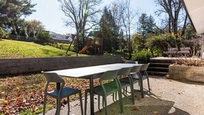 Ein Sitzbereich im Freien mit Tisch und Stühlen, im Hintergrund ein Spielplatz und eine sanfte Grasfläche.