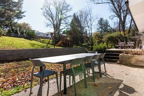 An outdoor seating area with a table and chairs, a playground in the background, and a grassy slope. - Aalto Modern - Spacious, 5-bed MCM - A Luxury KY Derby Vacation! (Louisville)