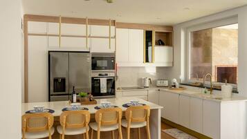 A modern kitchen with a central island, white cabinetry, stainless steel appliances, and a large window providing natural light.