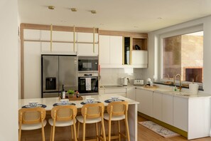 Una cocina moderna con una isla central, armarios blancos, electrodomésticos de acero inoxidable y un amplio ventanal que proporciona luz natural.