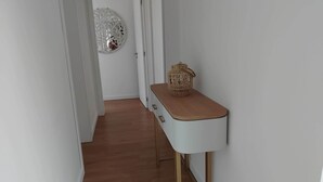 A hallway with a white wall, a wooden floor, a white cabinet with drawers, and a decorative wall hanging. - Casa das Hortênsias (Nossa Senhora do Pilar Terceira)