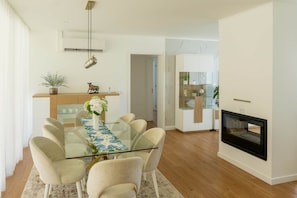 A modern dining area with a glass table, beige chairs, and a white wall.