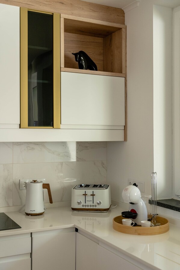 A kitchen with white cabinets, a wooden shelf, a toaster, a kettle, and a coffee maker.