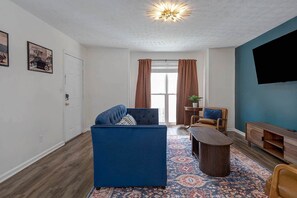 Ein Wohnzimmer mit einem blauen Sofa, einem Couchtisch und einem an einer blauen Wand montierten Fernseher.