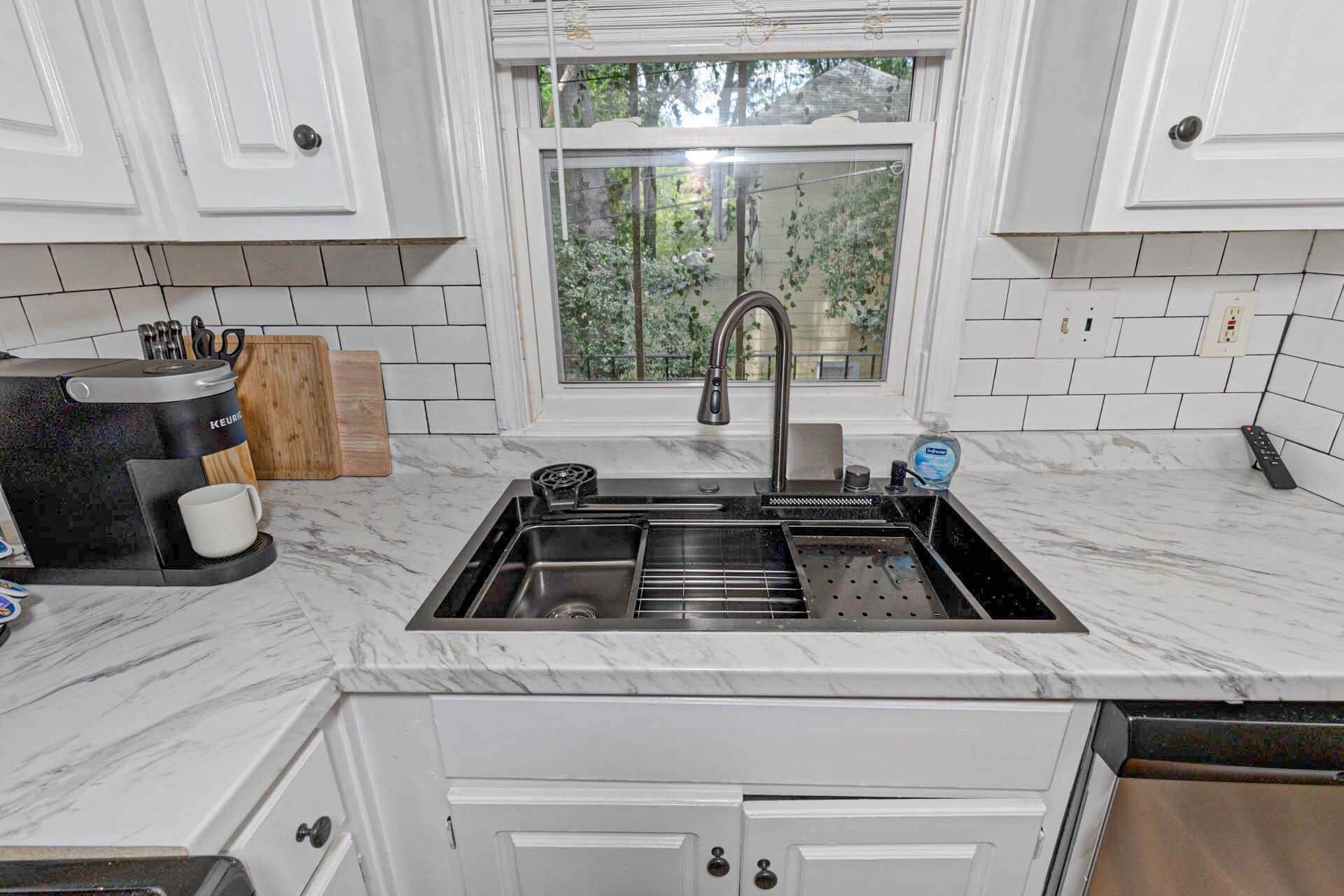 A kitchen with a built-in sink, a coffee maker, and a window with a view of greenery.