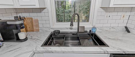 Una cocina con pileta integrada, cafetera y ventana con vista a la vegetación.