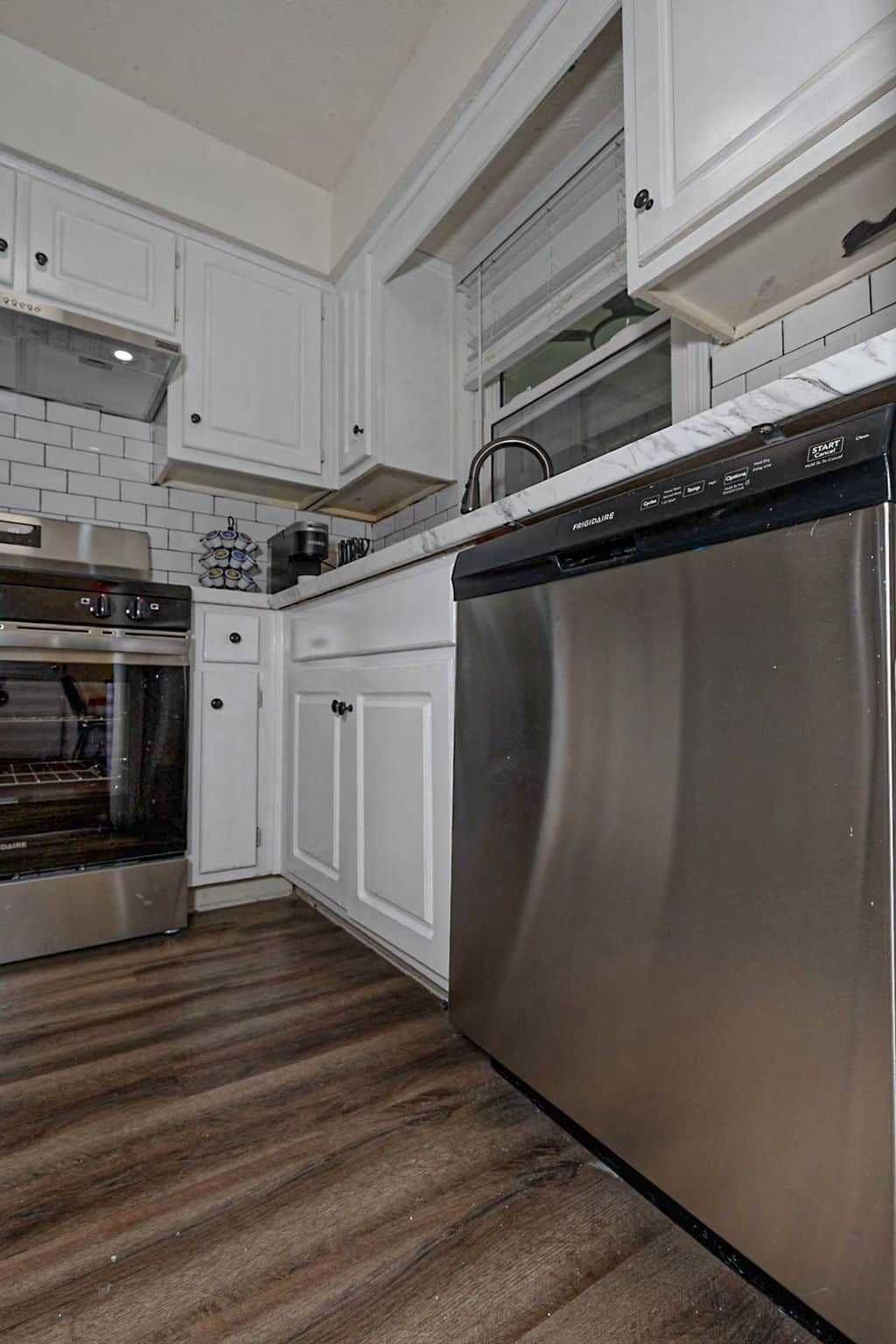 A kitchen with white cabinets, a stainless steel dishwasher, and a built-in oven.