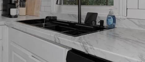 Una cocina con armarios blancos, un grifo negro y un lavavajillas.