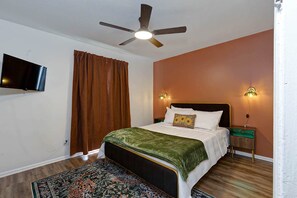 Ein Schlafzimmer mit einem Bett, einem Deckenventilator, einem an der Wand montierten Fernseher und zwei Nachttischlampen.