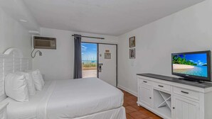 A hotel room with a bed, a television, a window with a view of the beach, and a door leading outside. - Sea Mist 20102 Ocean Front Condo (Myrtle Beach)