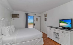 Ein Hotelzimmer mit Bett, Fernseher, Fenster mit Blick auf den Strand und einer Tür zum Ausgang.