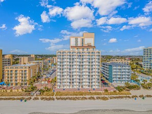Ein Hochhaus-Hotel mit mehreren Balkonen, einem Parkplatz und Blick auf den Strand.