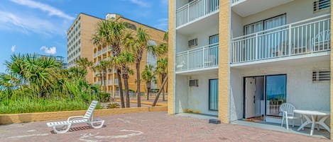 A hotel courtyard with a brick floor, palm trees, and a poolside area with lounge chairs.