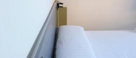 Ein Einzelbett mit weißer Bettwäsche in einem Zimmer mit schlichter Wand und einer Tür.