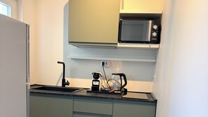 Een kleine keuken met een magnetron, koffiezetapparaat en een spoelbak.