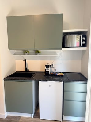 Cocina compacta con microondas integrado, un refrigerador pequeño y un lavamanos.