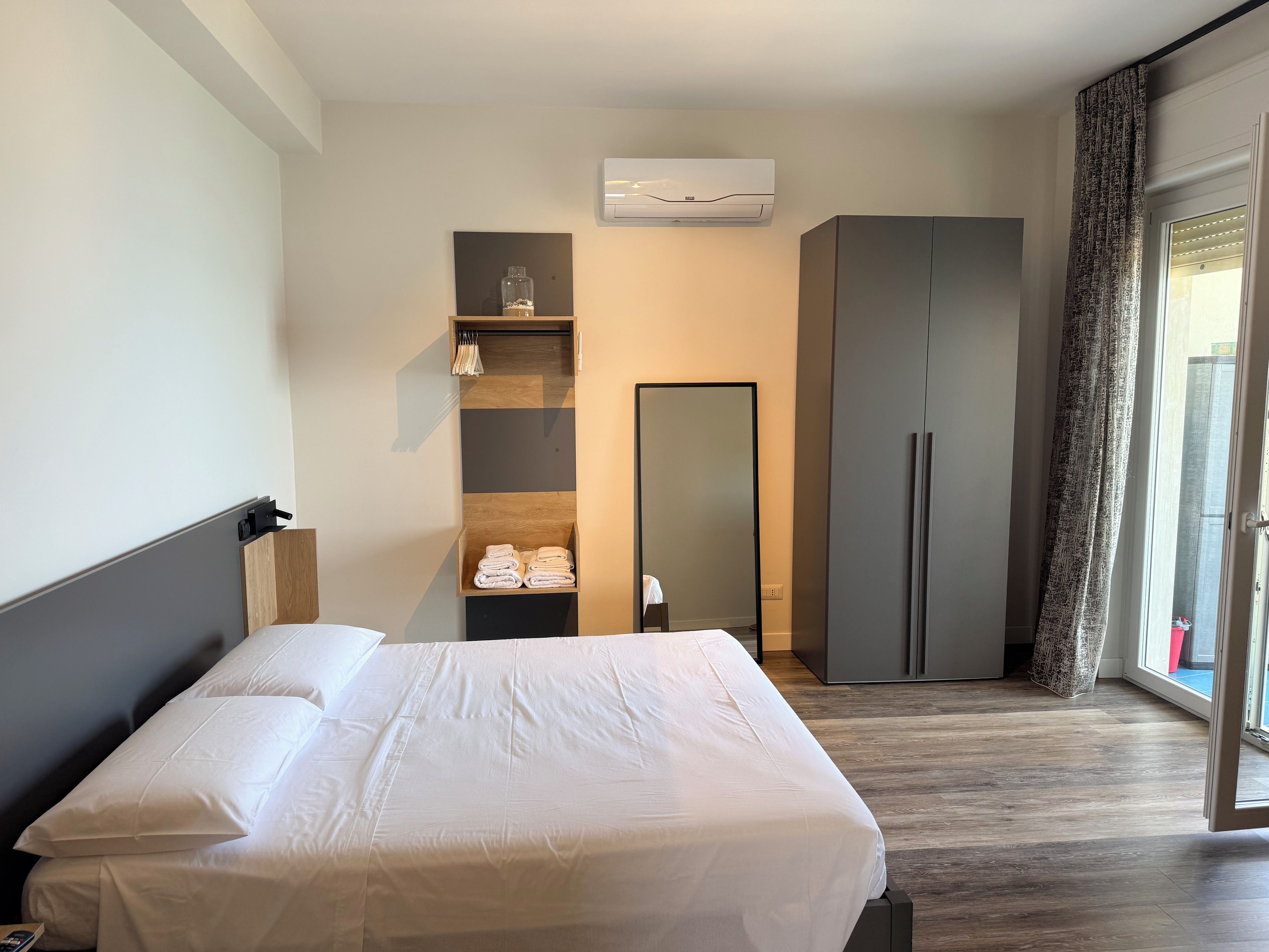 A hotel room with a bed, a wardrobe, a mirror, and a window with curtains.